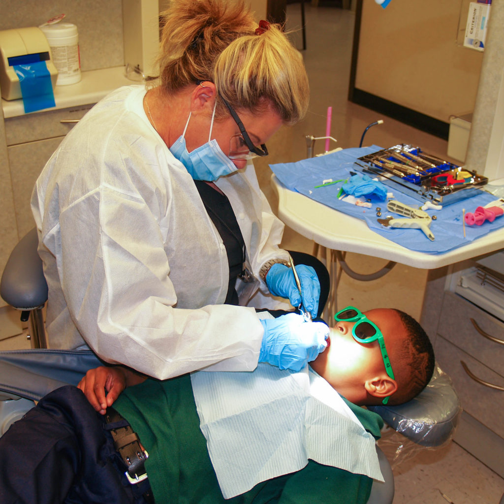 Dental hygienists performing a cleaning on a child.